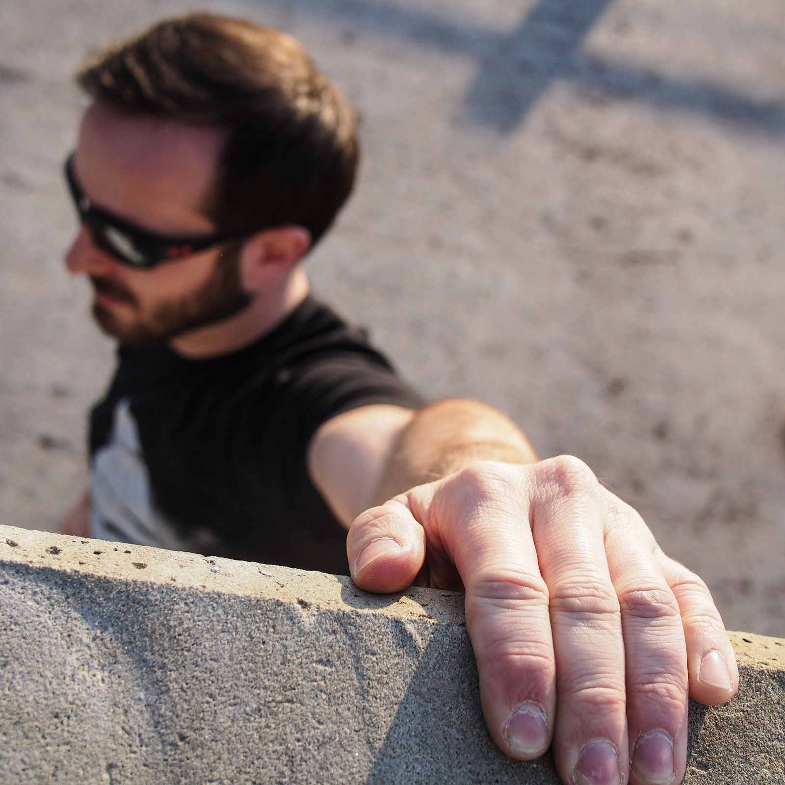 Daniel Williams in sunglasses, reaching toward the camera over a stone wall.