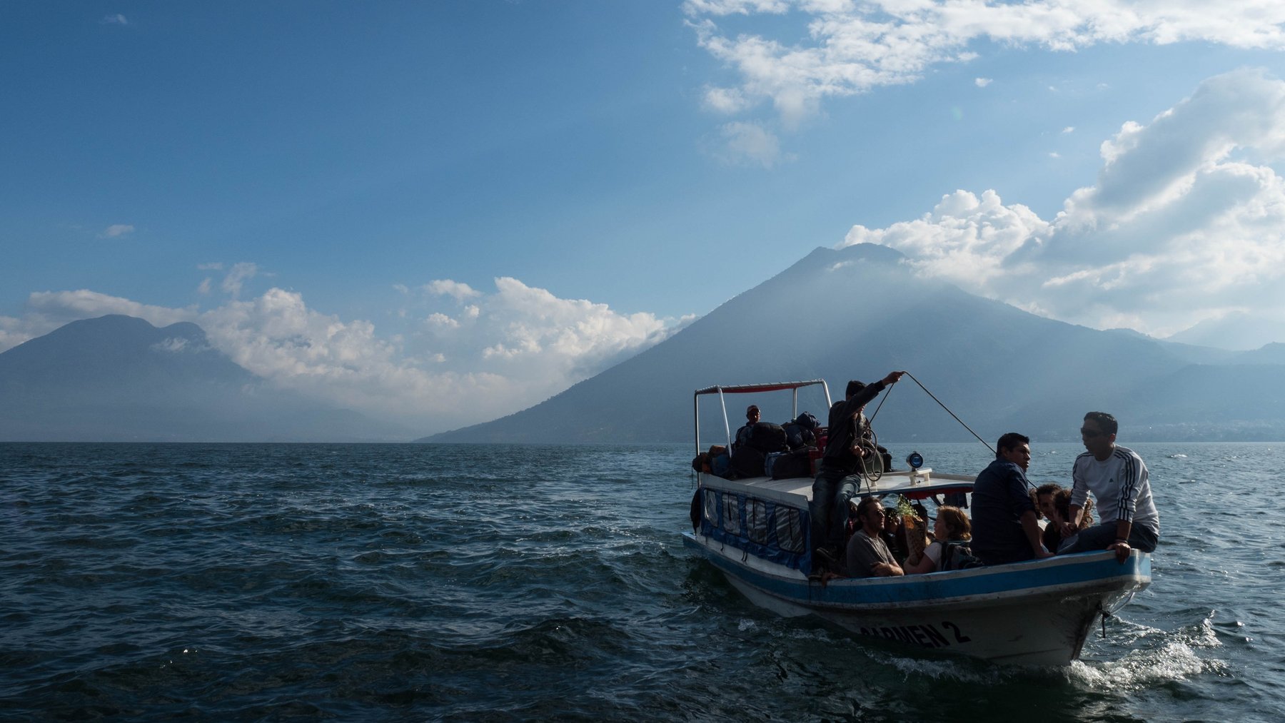 A small passenger boat on a lake below a hazy mountain.