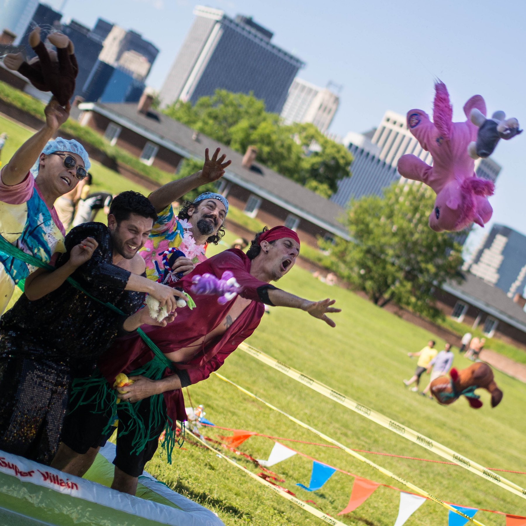 Colorfully costumed performers on a lawn with city buildings in the distance.