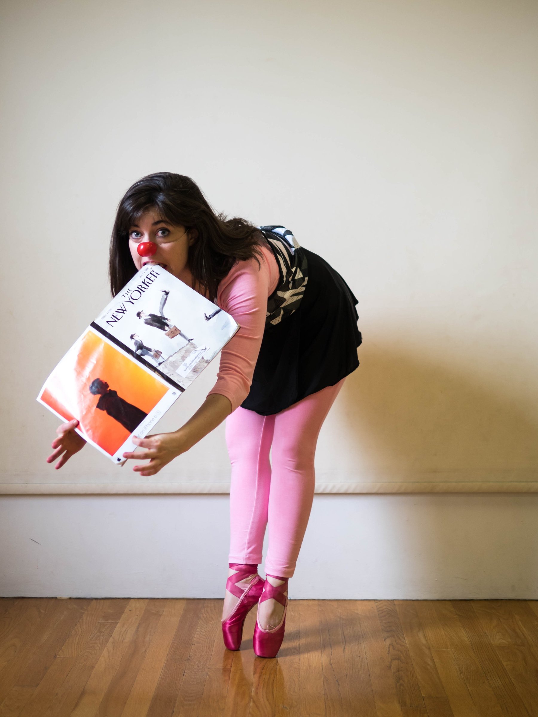 A performer in pink tights bending forward while holding a box.