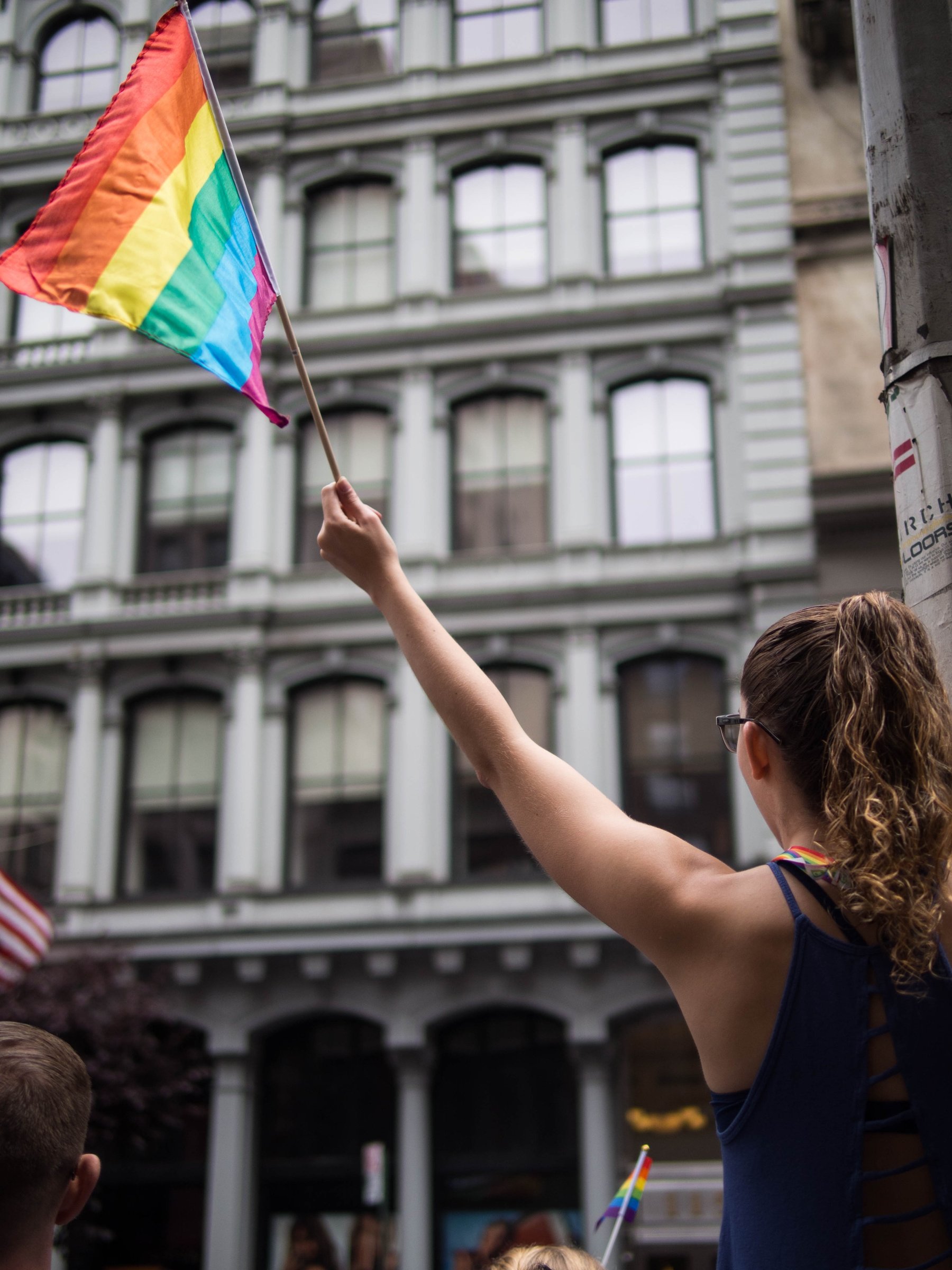 A person raising a rainbow flag in front of an ornate city building.